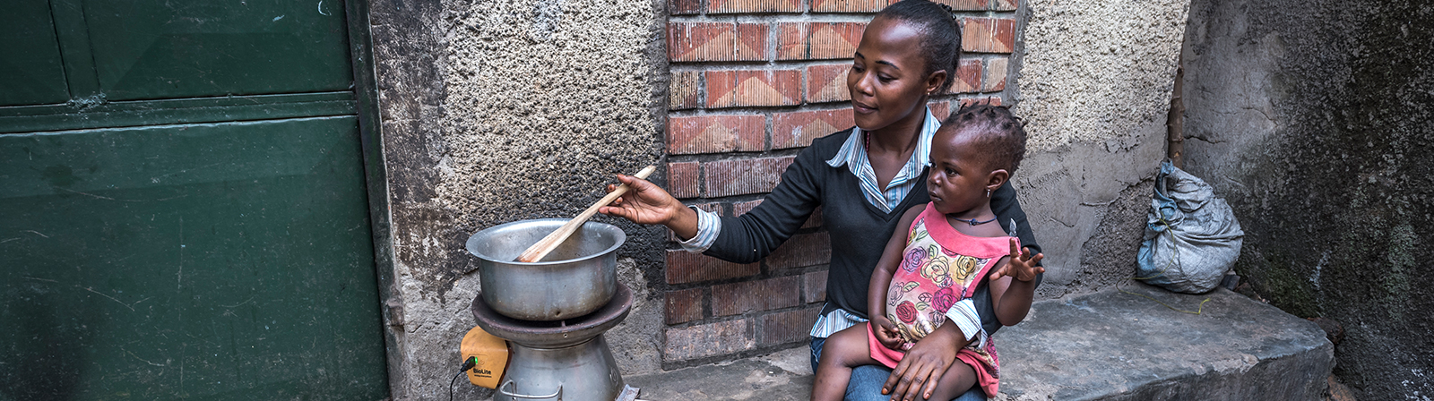 woman and child sitting outside their home cooking